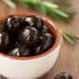 A small bowl filled with black olives placed on a wooden surface. - Olive Oil Times