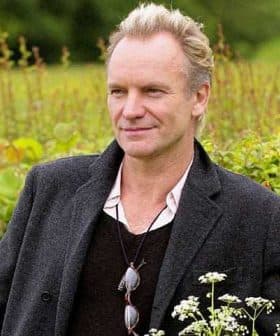 Man wearing a black coat and sunglasses, standing outdoors with greenery in the background. - Olive Oil Times