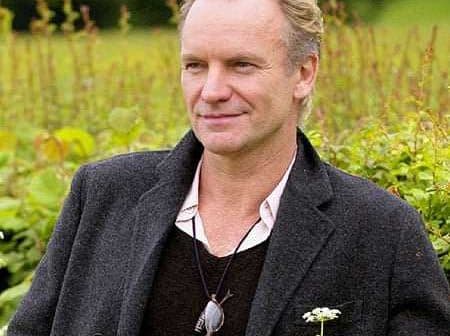 Man wearing a black coat and sunglasses, standing outdoors with greenery in the background. - Olive Oil Times