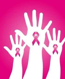 Three white hands raised with pink ribbons symbolizing breast cancer awareness. - Olive Oil Times
