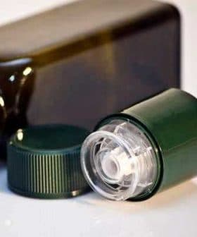 Green plastic bottle with a removable cap placed next to it on a white surface. - Olive Oil Times