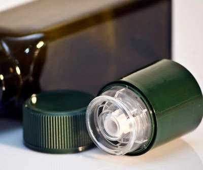 Green plastic bottle with a removable cap placed next to it on a white surface. - Olive Oil Times