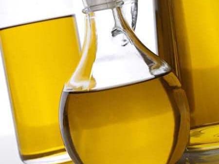 Glass cruet filled with olive oil, surrounded by two additional bottles of oil. - Olive Oil Times