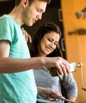 A man and a woman pouring olive oil while cooking in a kitchen setting. - Olive Oil Times