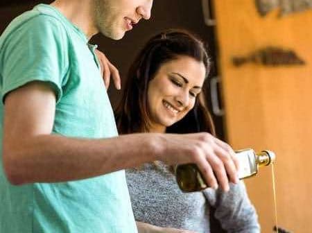 A man and a woman pouring olive oil while cooking in a kitchen setting. - Olive Oil Times
