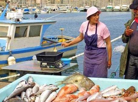 Woman and man at a fish market in Marseille with a large display of fresh fish. - Olive Oil Times