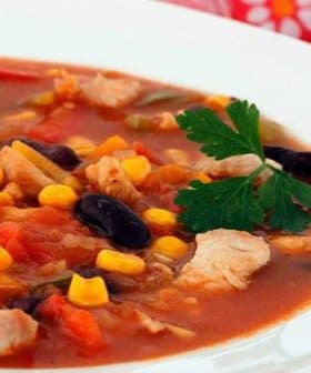 Bowl of chicken and vegetable soup with corn, beans, and herbs on a white plate. - Olive Oil Times