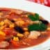 Bowl of chicken and vegetable soup with corn, beans, and herbs on a white plate. - Olive Oil Times