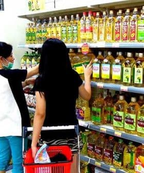 Two individuals shopping for cooking oils on a supermarket shelf filled with various oil bottles. - Olive Oil Times