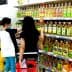 Two individuals shopping for cooking oils on a supermarket shelf filled with various oil bottles. - Olive Oil Times