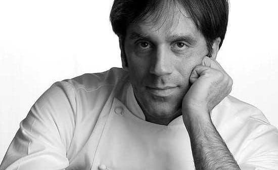 Black and white portrait of a chef resting his chin on his hand, wearing a white chef's uniform. - Olive Oil Times