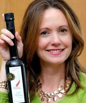 Woman smiling while holding a bottle of olive oil in her right hand. - Olive Oil Times