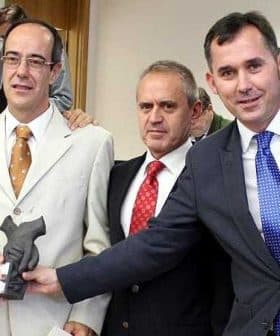 Three men standing together, one holding a trophy, in a formal setting. - Olive Oil Times