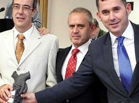 Three men standing together, one holding a trophy, in a formal setting. - Olive Oil Times