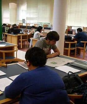 Students engaged in reading and studying at tables in a library setting. - Olive Oil Times