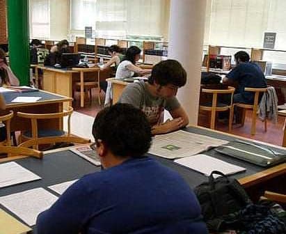 Students engaged in reading and studying at tables in a library setting. - Olive Oil Times