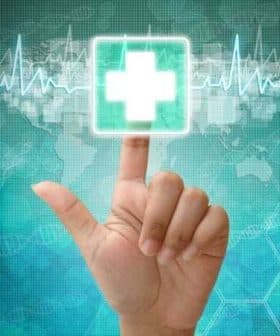A hand pointing at a digital health icon featuring a medical cross on a blue background. - Olive Oil Times