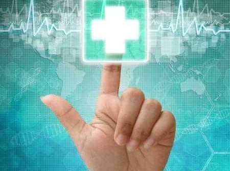 A hand pointing at a digital health icon featuring a medical cross on a blue background. - Olive Oil Times