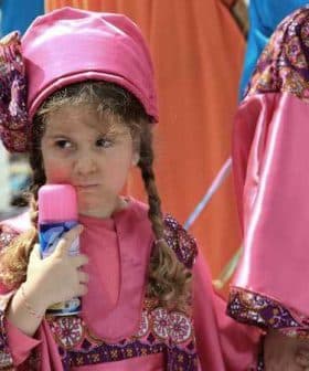 Young girl wearing a pink traditional costume holding a colorful toy in her hand. - Olive Oil Times