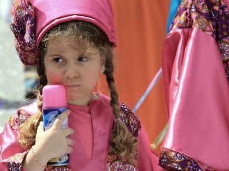 Young girl wearing a pink traditional costume holding a colorful toy in her hand. - Olive Oil Times