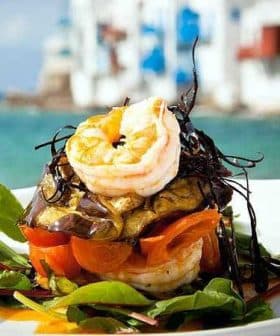 A layered dish featuring shrimp, vegetables, and greens presented on a plate. - Olive Oil Times