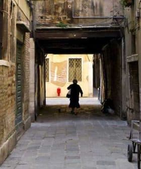 Individual walking through a narrow alleyway with brick walls and a cat following. - Olive Oil Times
