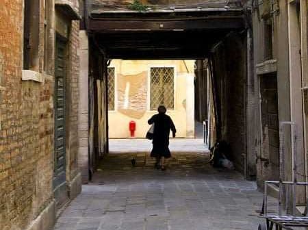 Individual walking through a narrow alleyway with brick walls and a cat following. - Olive Oil Times