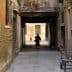 Individual walking through a narrow alleyway with brick walls and a cat following. - Olive Oil Times