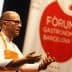 A chef gesturing while speaking at the Gastronomy Forum in Barcelona, wearing an orange apron. - Olive Oil Times