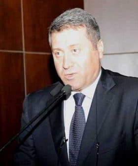 A man in a suit speaking into a microphone at a podium during an event. - Olive Oil Times