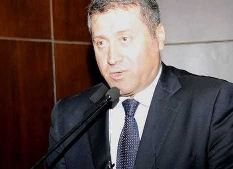 A man in a suit speaking into a microphone at a podium during an event. - Olive Oil Times