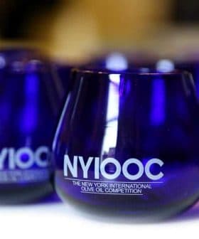 Blue glasses with the NYIOOC logo for the New York International Olive Oil Competition. - Olive Oil Times