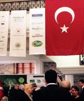 Turkish flag with a white star and crescent displayed at an indoor event with attendees. - Olive Oil Times