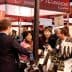 Group of people engaging in conversation at a wine tasting event with bottles displayed. - Olive Oil Times