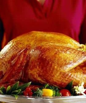 A person holding a large roasted turkey on a silver serving platter with garnishes. - Olive Oil Times