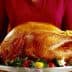 A person holding a large roasted turkey on a silver serving platter with garnishes. - Olive Oil Times