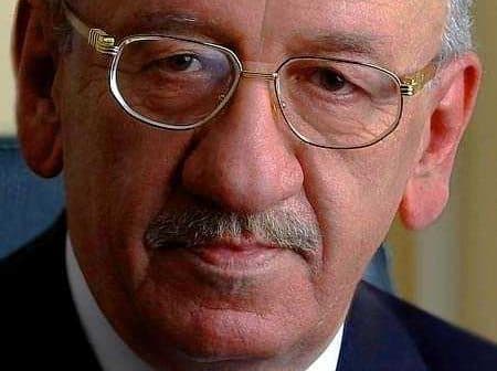 Close-up portrait of an older man wearing glasses and a suit with a serious expression. - Olive Oil Times