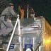 Two law enforcement officers climbing a ladder to inspect the top of a truck at night. - Olive Oil Times