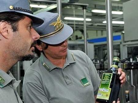 Two individuals examining a bottle of olive oil in a production facility. - Olive Oil Times