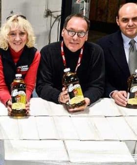 Three individuals holding bottles of olive oil in a warehouse setting. - Olive Oil Times