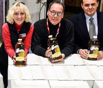 Three individuals holding bottles of olive oil in a warehouse setting. - Olive Oil Times