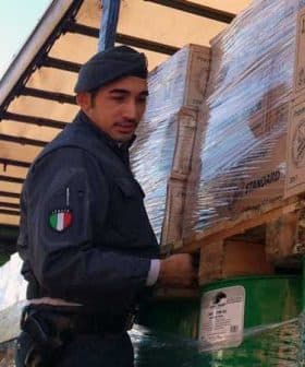 Italian police officer in uniform managing cargo on a truck with boxes and pallets. - Olive Oil Times