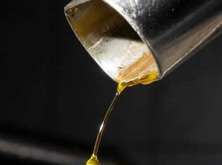 A close-up view of olive oil dripping from a metal spout into a container. - Olive Oil Times