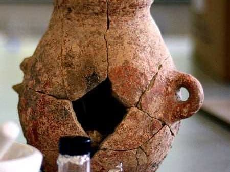 An ancient clay pot with visible cracks and a handle, displaying signs of age and wear. - Olive Oil Times
