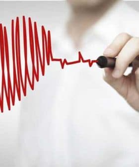 Person's hand drawing a red heartbeat line with a marker on a white background. - Olive Oil Times