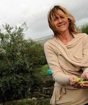 Woman with long hair wearing a beige sweater, holding olives in her hands in an outdoor setting. - Olive Oil Times