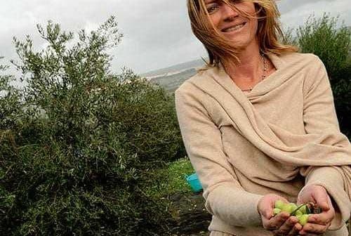 Woman with long hair wearing a beige sweater, holding olives in her hands in an outdoor setting. - Olive Oil Times