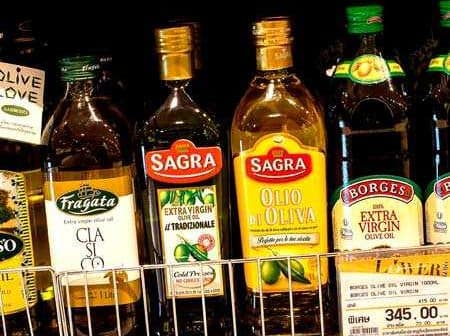 Different brands of olive oil bottles displayed on a supermarket shelf. - Olive Oil Times