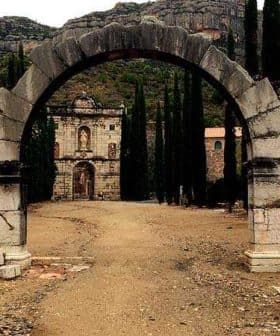 Archway with a stone structure visible in the background, surrounded by tall trees. - Olive Oil Times