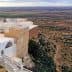 Aerial view of a landscape in Tunisia featuring olive groves and a building on a cliff edge. - Olive Oil Times